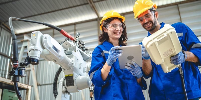 Técnicos industriales revisando información junto a un robot de fábrica